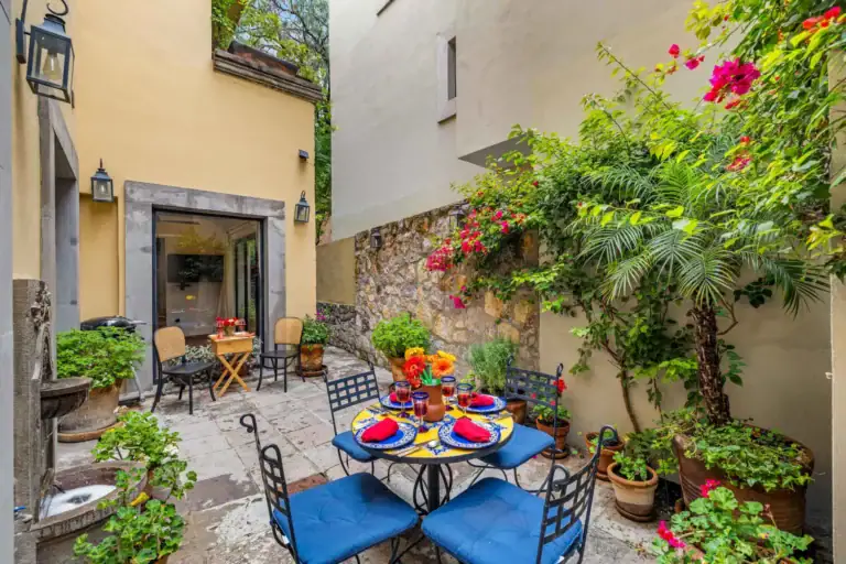 Casa Paradise, courtyard dining table with blue chairs beside a stone wall fountain, San Miguel de Allende