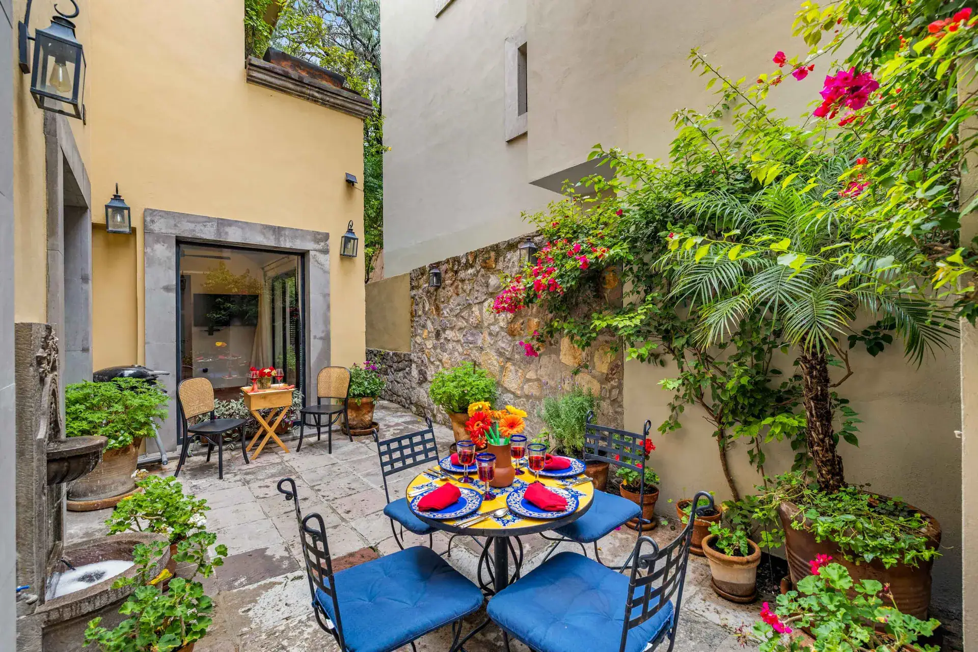 Casa Paradise, courtyard dining table with blue chairs beside a stone wall fountain, San Miguel de Allende