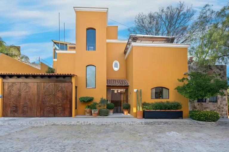 Casa Privada, ochre house with a tower, a carved wooden garage door and a front gate on a cobblestone lane, San Miguel de Allende
