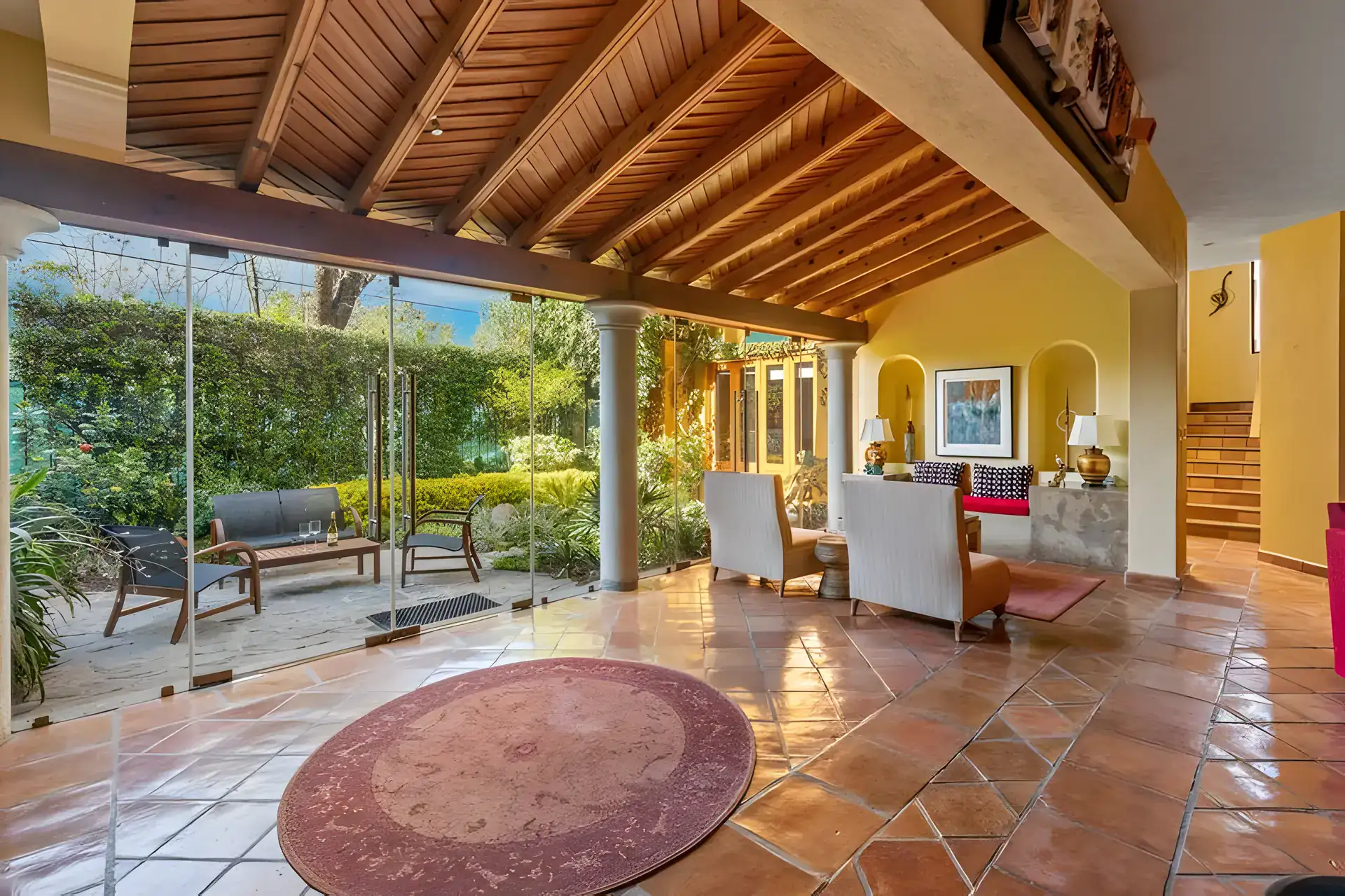 Casa Privada, covered patio with a wood-beam ceiling and glass walls to the garden, next to a sitting area, San Miguel de Allende