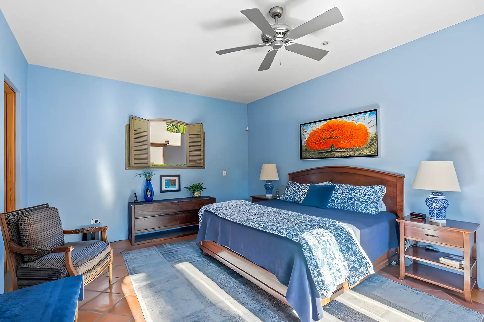 Casa Privada, bedroom with blue walls, a wood bed, a bright painting and a window with shutters, San Miguel de Allende