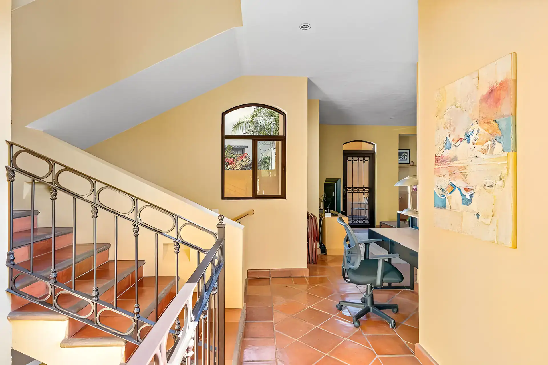 Casa Privada, upstairs landing with an iron stair railing, a home office desk and an arched window, San Miguel de Allende