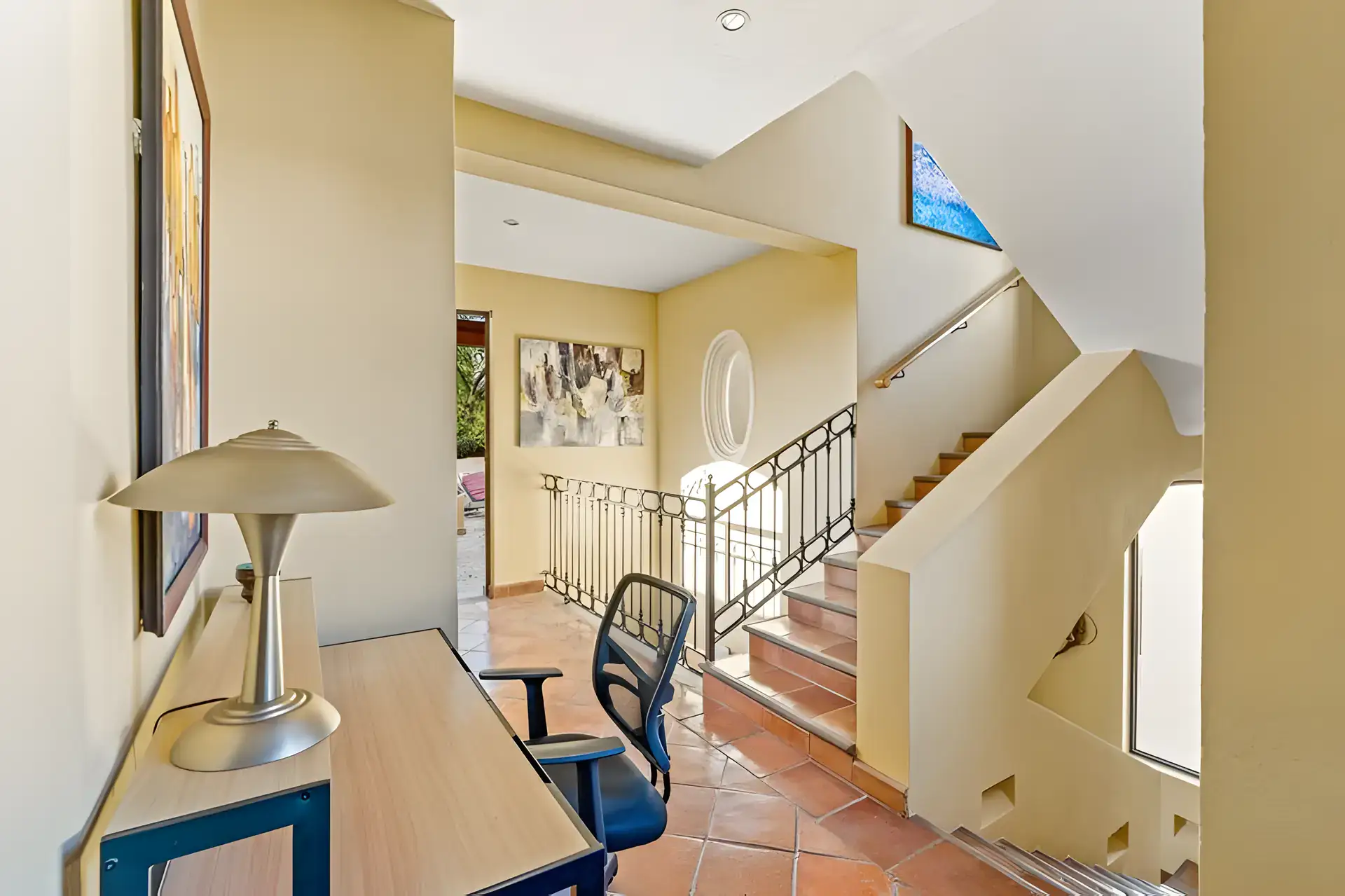 Casa Privada, landing with a desk and chair at a stairwell with an oval window and a wrought-iron railing, San Miguel de Allende