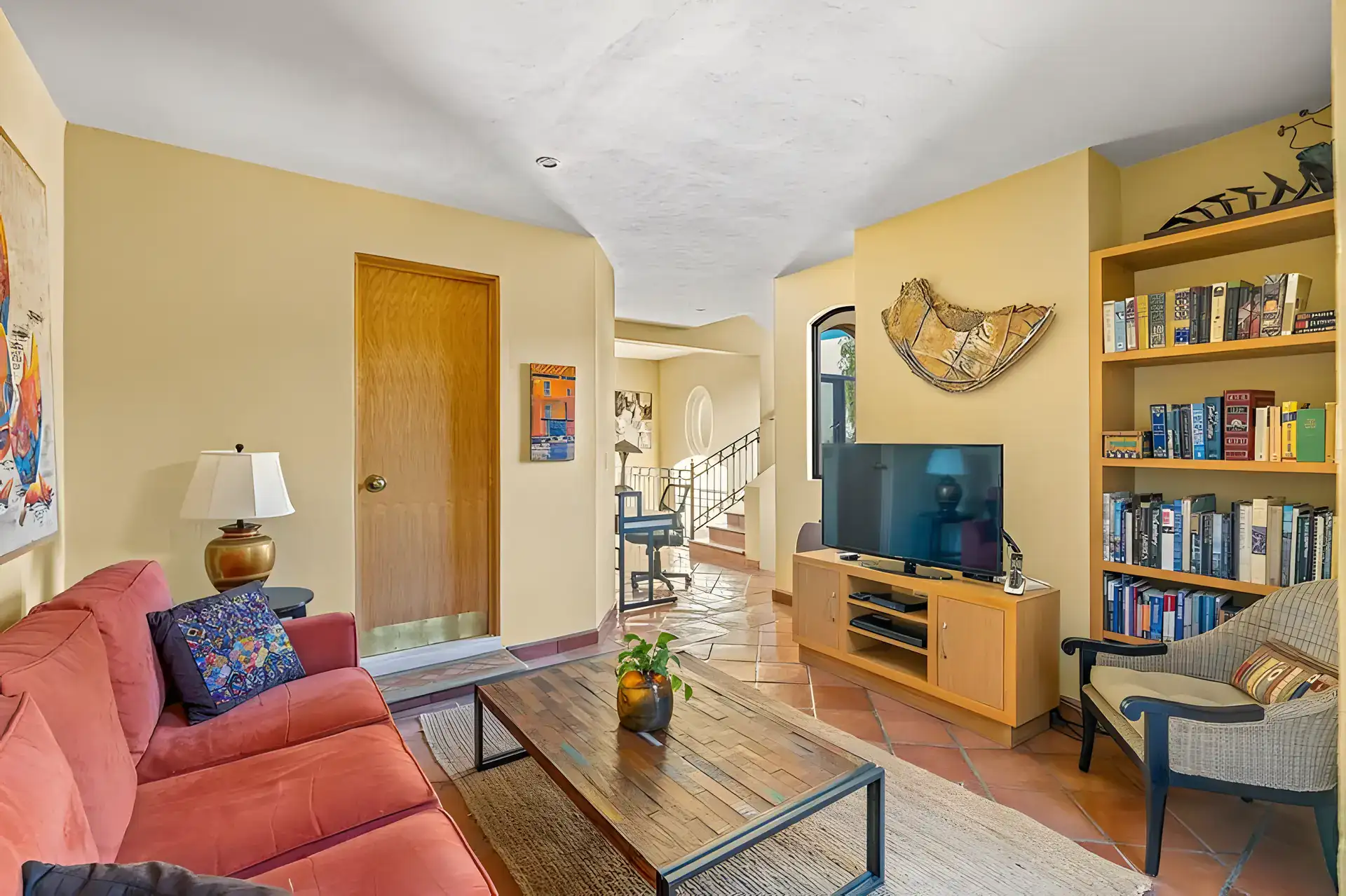 Casa Privada, den with a coral sofa, a television, bookshelves and a view to the stairs, San Miguel de Allende