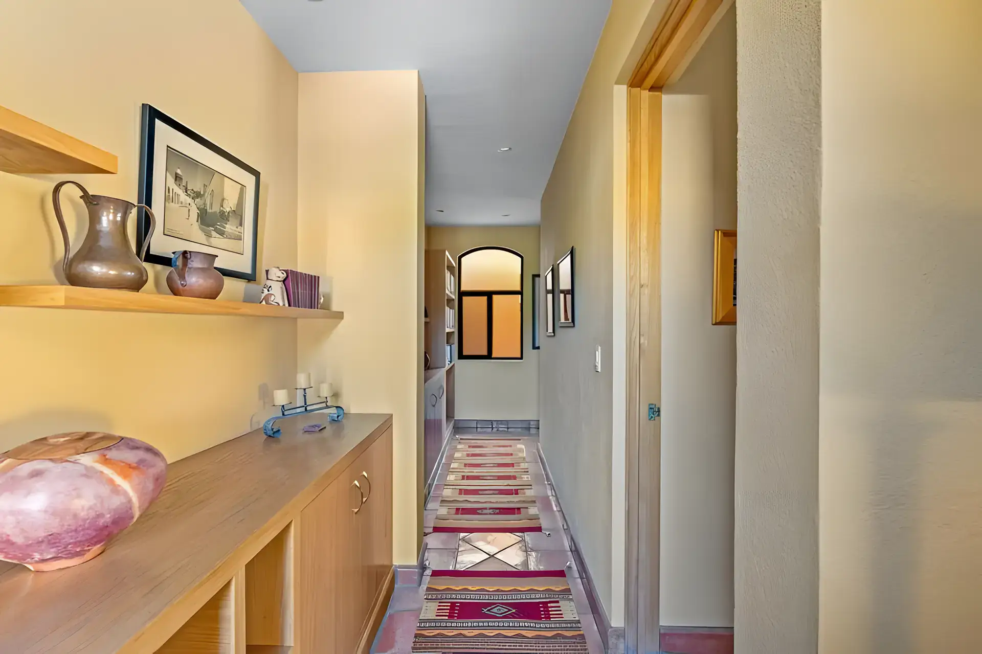 Casa Privada, hallway with a wood console, a copper pitcher, a runner rug and an arched window at the end, San Miguel de Allende