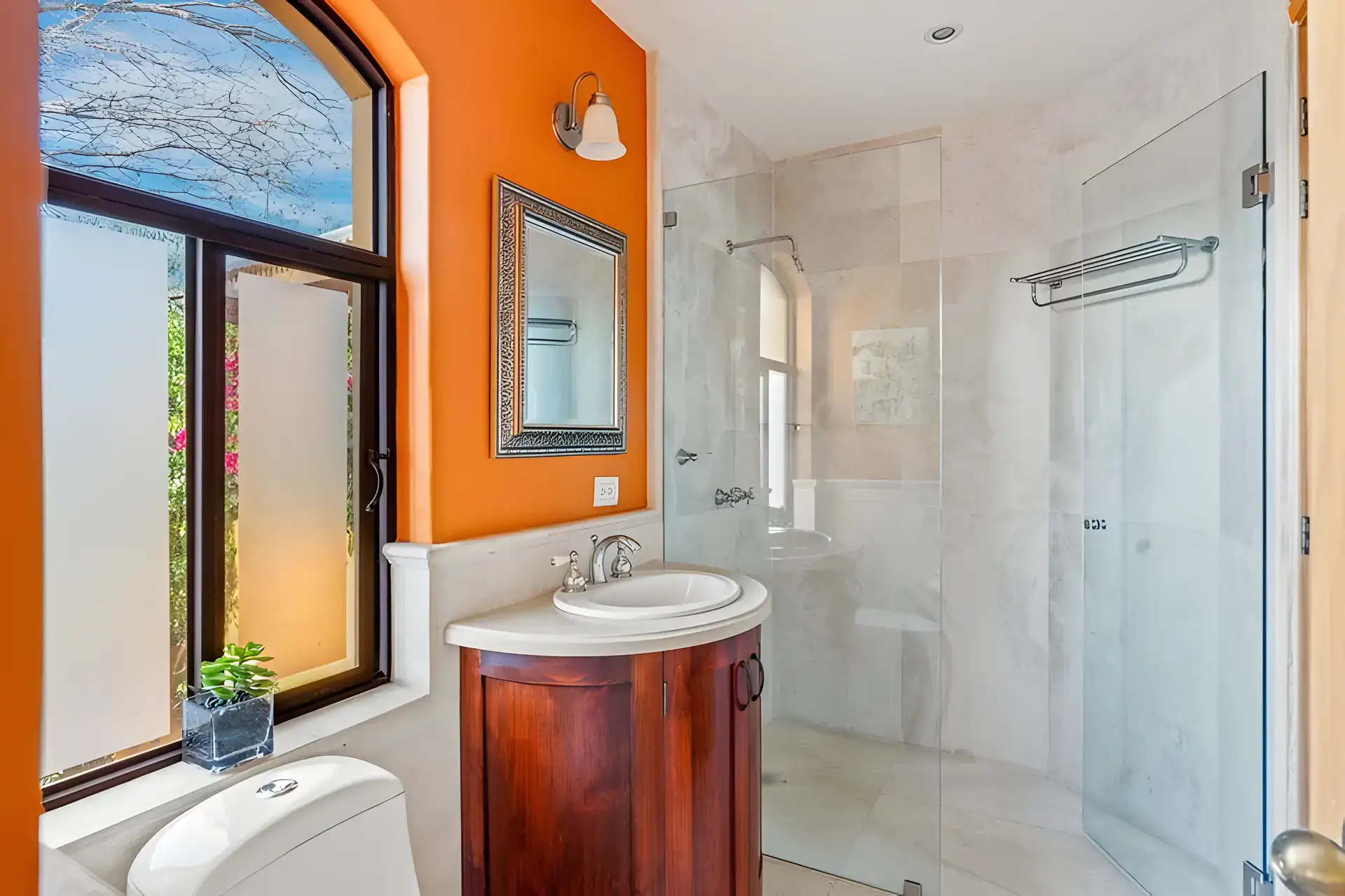 Casa Privada, bathroom with an orange wall, an arched window, a round vanity and a glass shower, San Miguel de Allende