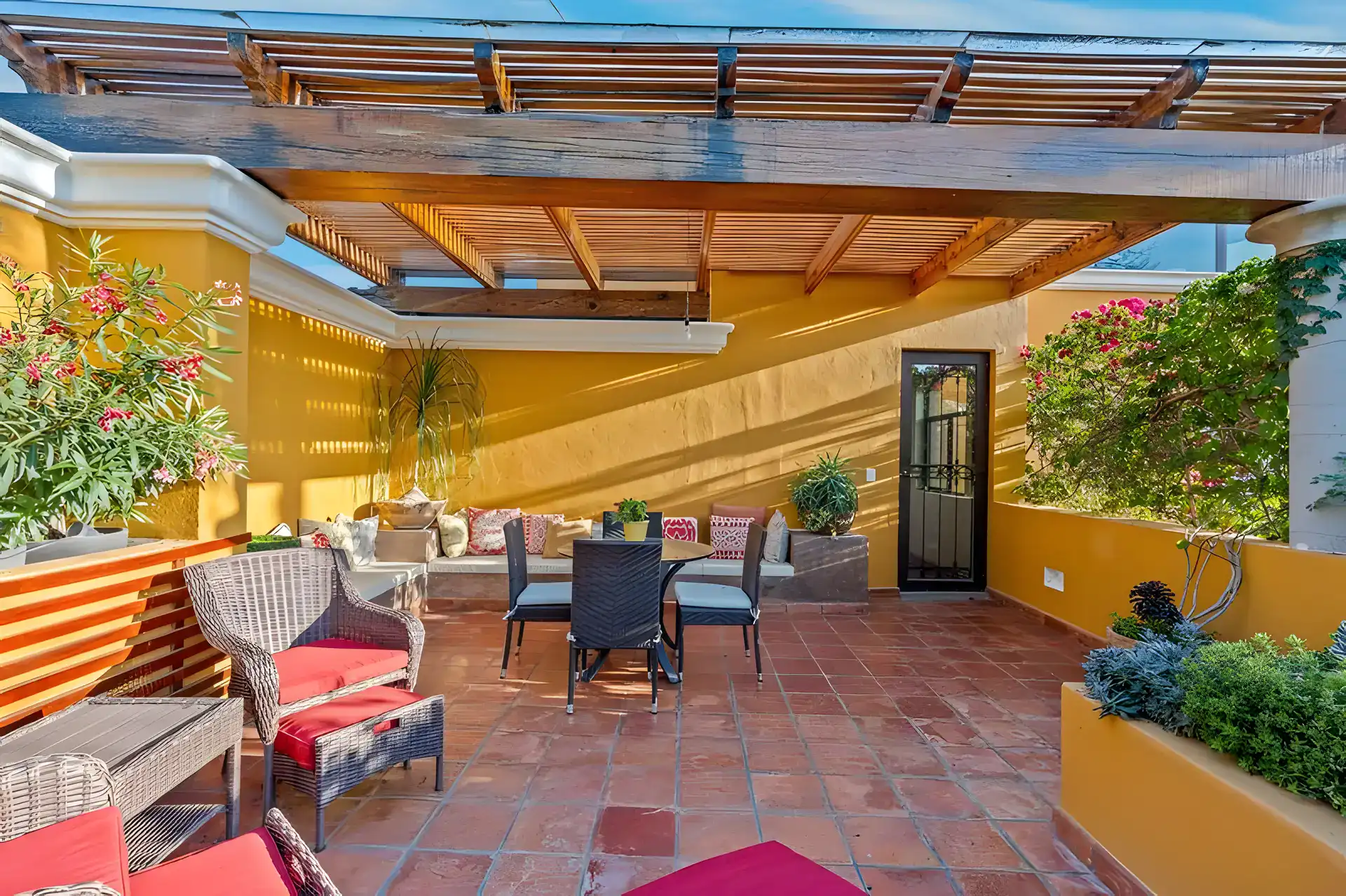 Casa Privada, rooftop terrace with a slatted pergola, wicker seating with red cushions and potted plants, San Miguel de Allende