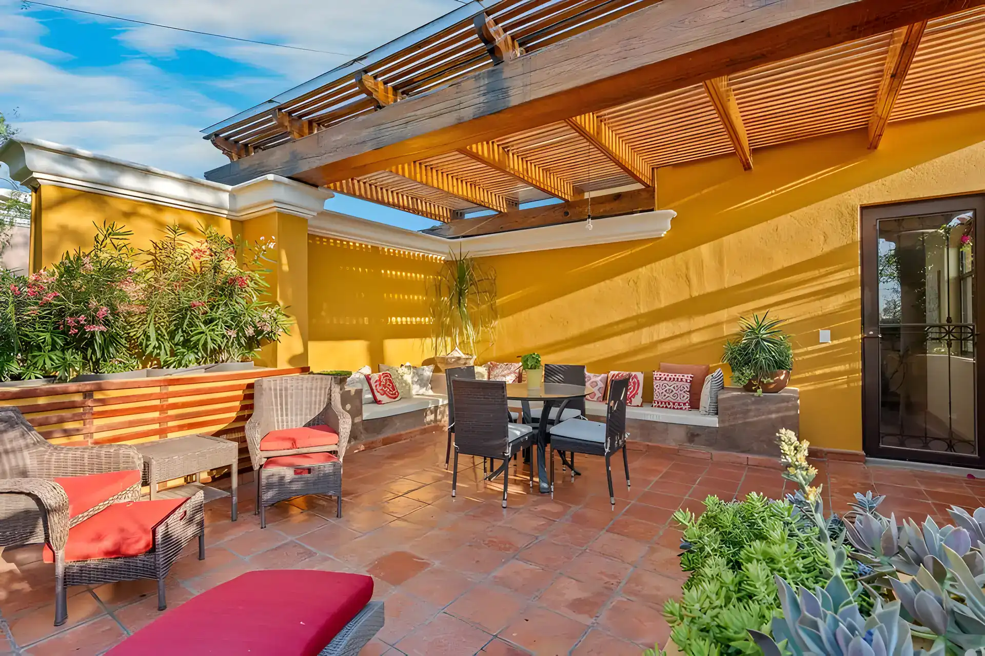 Casa Privada, rooftop terrace with a dining table, wicker chairs and planter beds under a wood slat roof, San Miguel de Allende