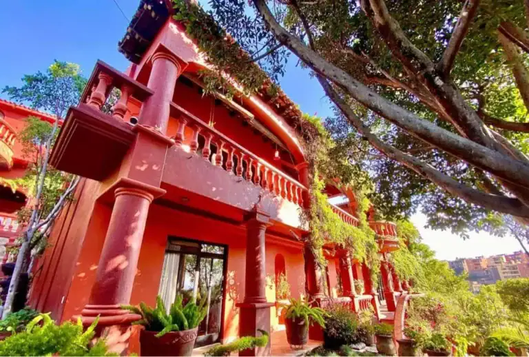 Casa Puesta del Sol, red house with balconies and columns beside a large tree, San Miguel de Allende