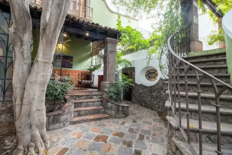 Casa Quetzal Hotel, courtyard with a spiral iron staircase, flagstone paving and a tree trunk beside a covered porch, San Miguel de Allende