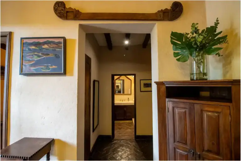 Casa Quetzal Hotel, hallway nook with a carved wood cabinet, a painting and a view to the bathroom, San Miguel de Allende