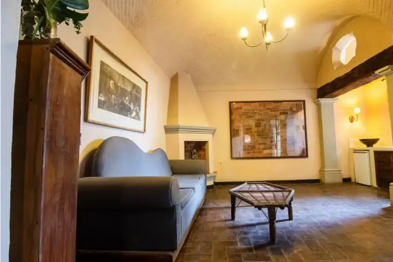 Casa Quetzal Hotel, suite with a gray sofa, corner fireplace and a vaulted ceiling with a chandelier, San Miguel de Allende