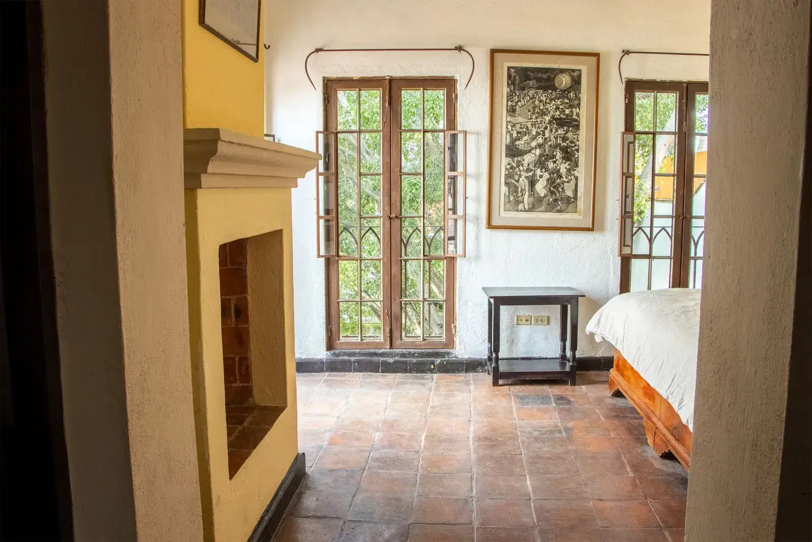 Casa Quetzal Hotel, bedroom with a fireplace, a tall window with a view of trees and a framed black-and-white print, San Miguel de Allende