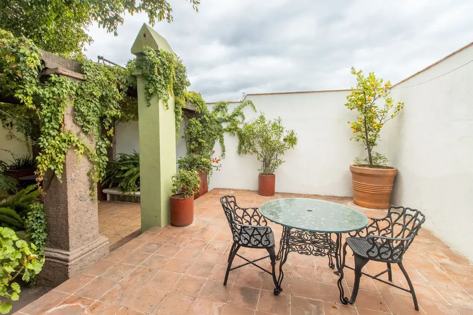 Casa Quetzal Hotel, terrace with a glass table and wrought-iron chairs beside a vine-covered column, San Miguel de Allende