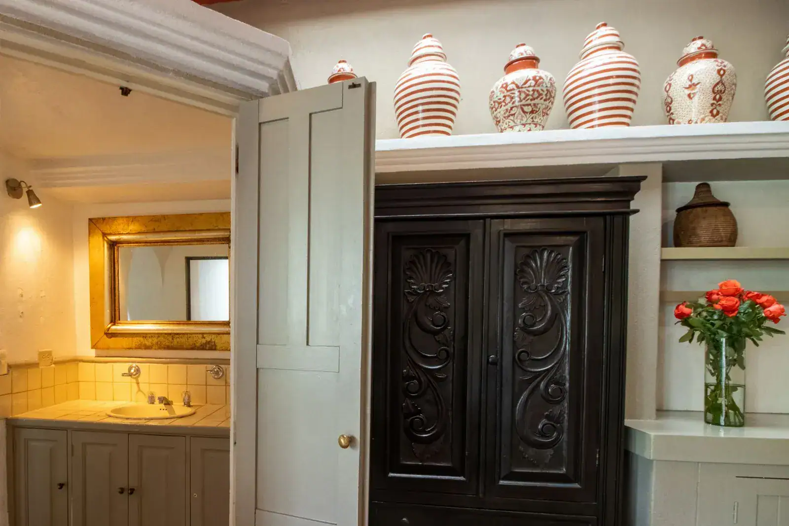 Casa Quetzal Hotel, bathroom vanity beside an ornate carved armoire and shelves of ceramic jars, San Miguel de Allende