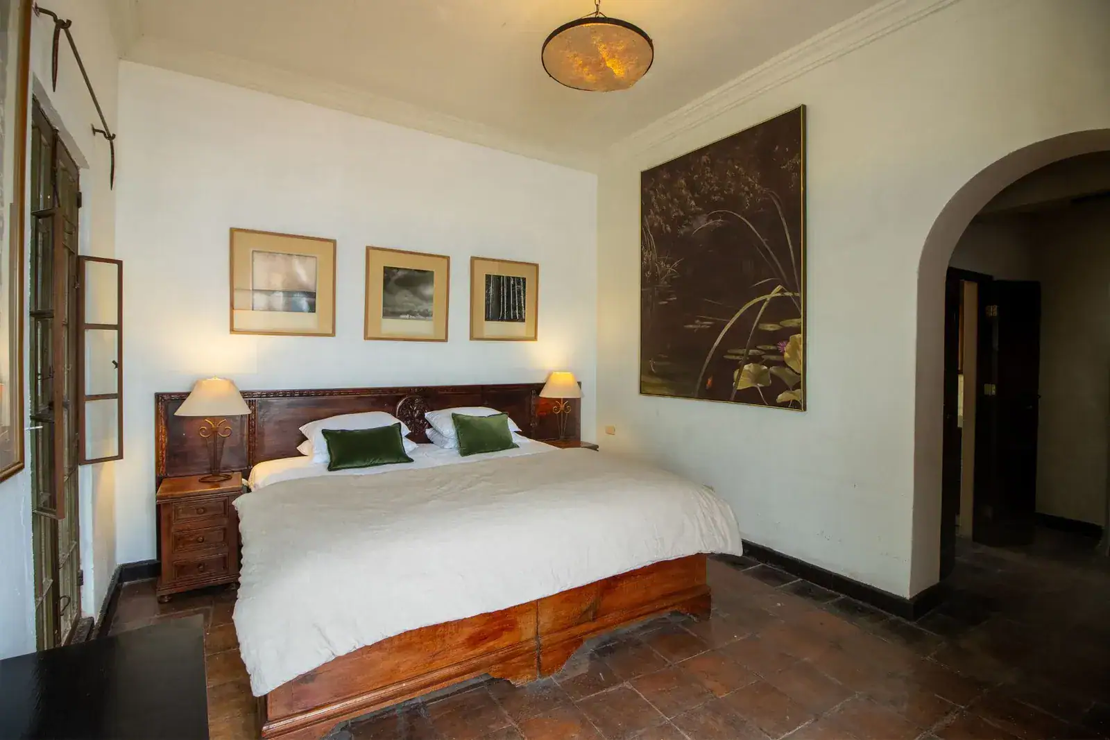 Casa Quetzal Hotel, bedroom with a carved wood bed, framed prints and an arched hallway, San Miguel de Allende