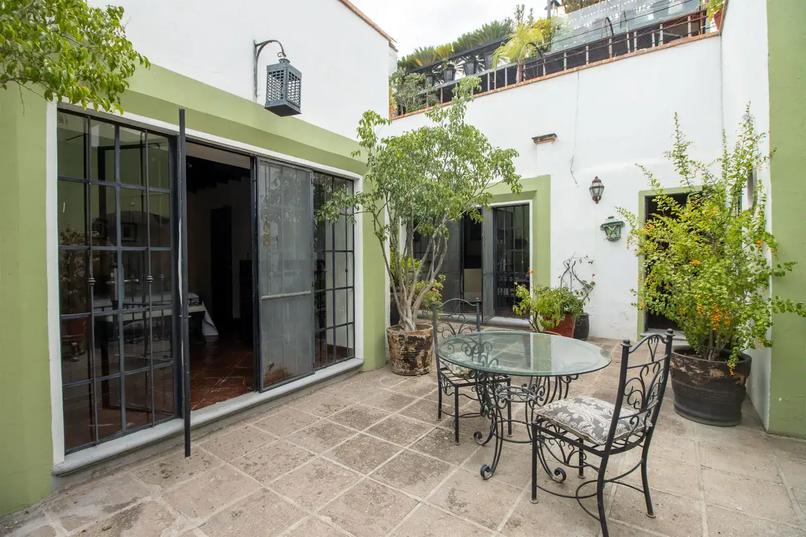 Casa Quetzal Hotel, patio with a glass table, black-framed glass doors and potted trees, San Miguel de Allende