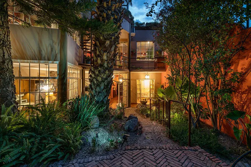 Casa Ro, courtyard garden with glowing windows at dusk among palms, San Miguel de Allende
