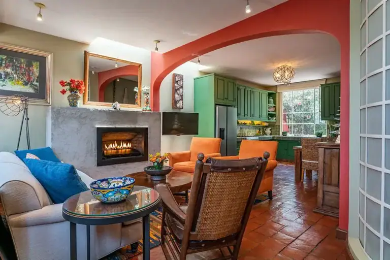 Casa Ro, sitting room with a fireplace, orange chairs and an arched opening, San Miguel de Allende