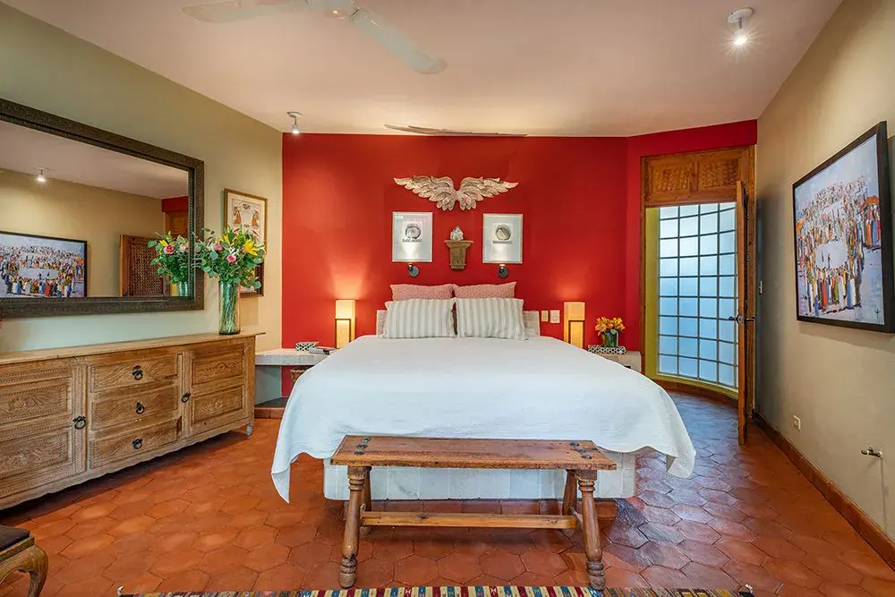 Casa Ro, primary bedroom with a red accent wall and a white bed, San Miguel de Allende