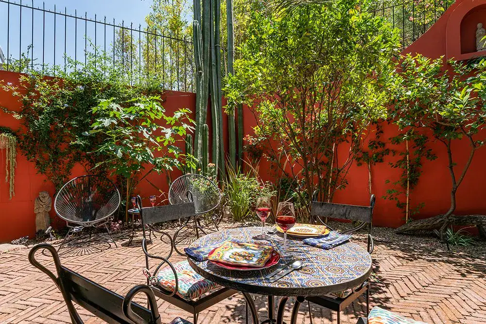 Casa Ro, brick courtyard with a mosaic table and chairs beside a red wall, San Miguel de Allende