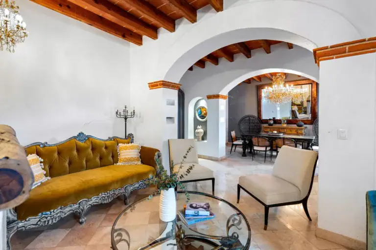 Casa Roka, living room with an ornate gold sofa and white chairs beside arched openings into the dining room, San Miguel de Allende