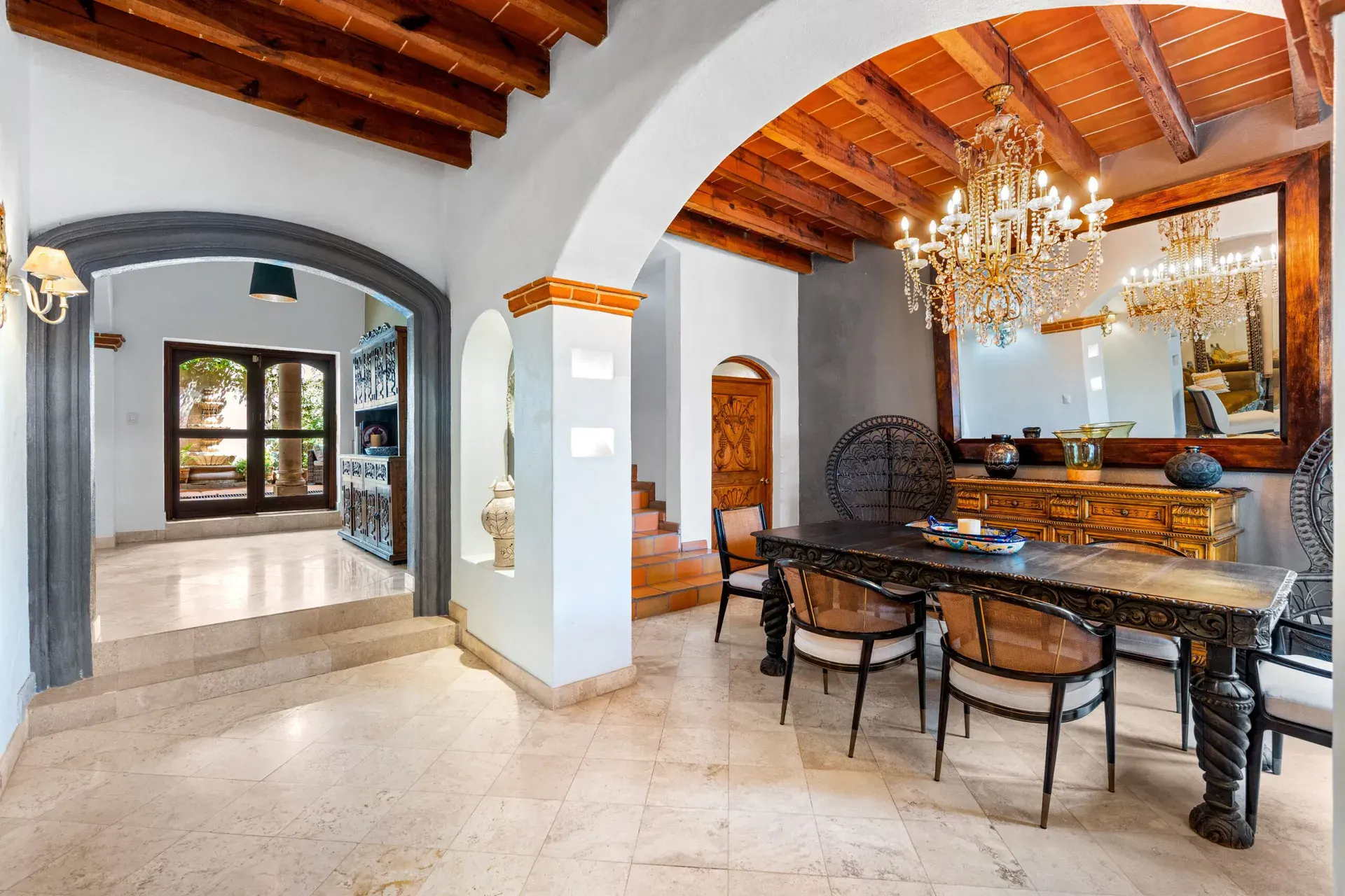 Casa Roka, dining room with a carved dark wood table, rattan chairs, a crystal chandelier and a large mirror, San Miguel de Allende