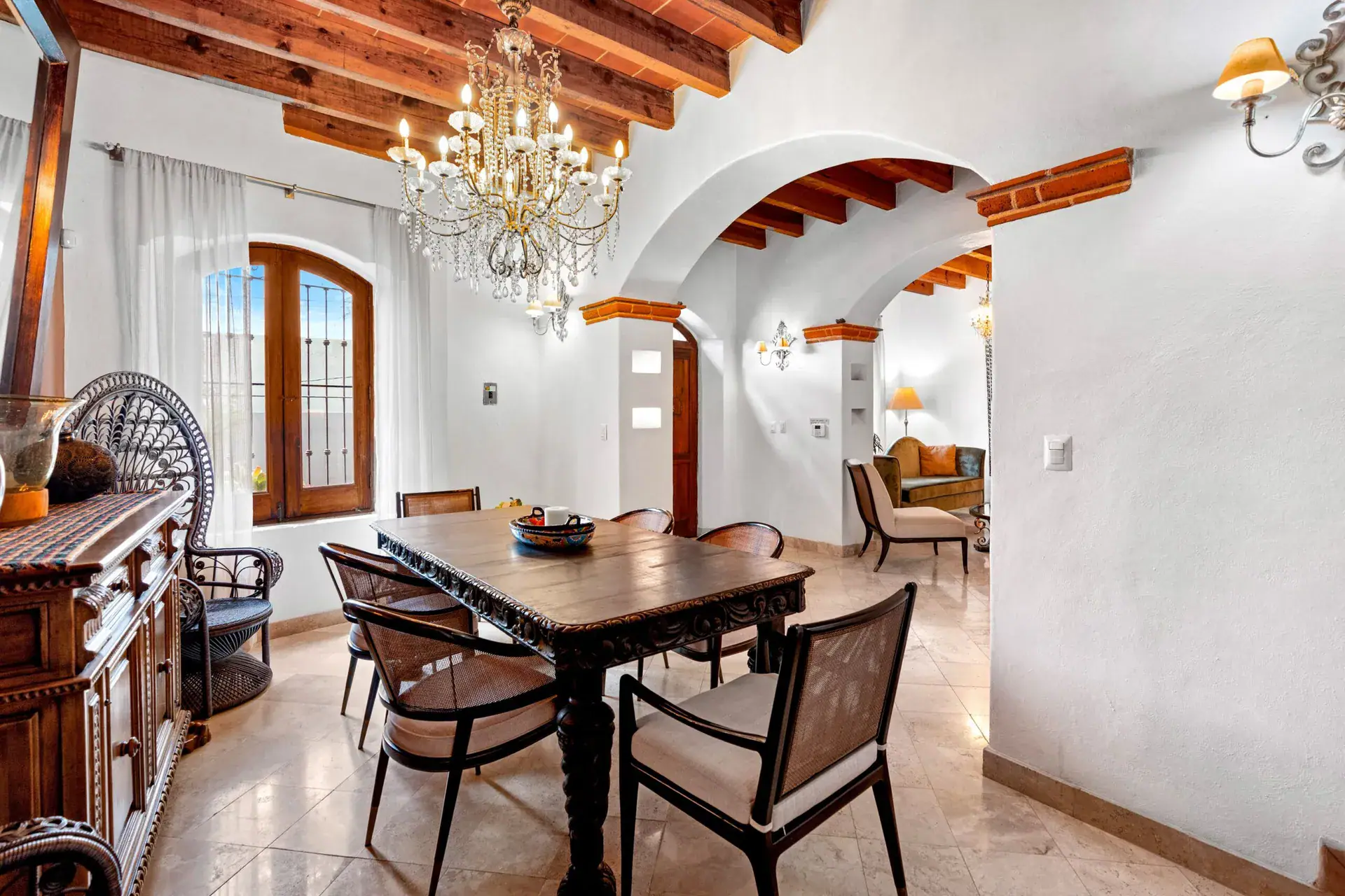 Casa Roka, dining room with a wood table and rattan chairs, a crystal chandelier and an arched window, San Miguel de Allende