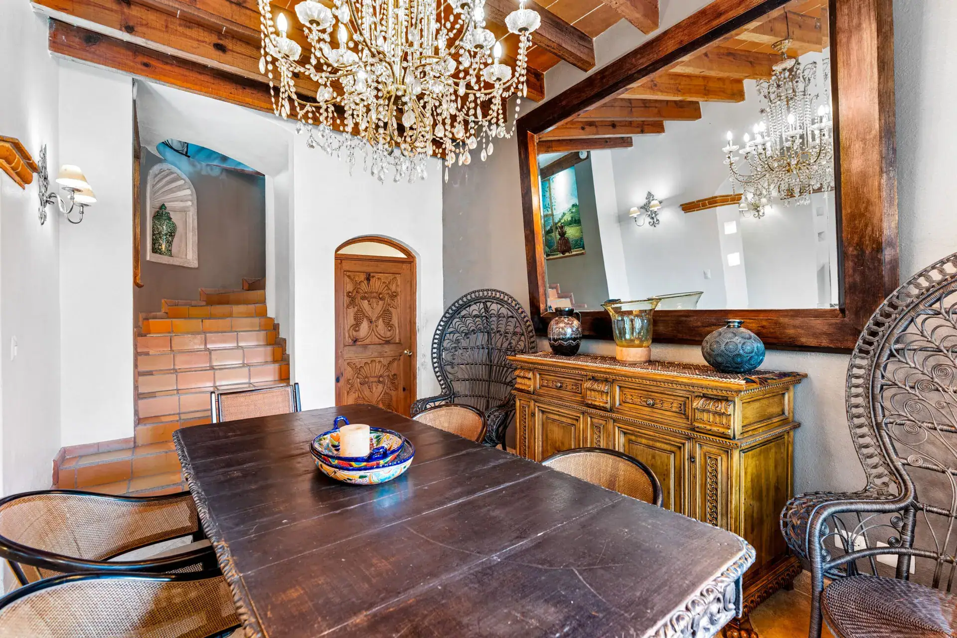 Casa Roka, dining table with a peacock chair, a carved sideboard, a large wood-framed mirror and a stair, San Miguel de Allende