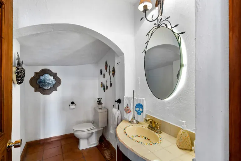 Casa Roka, powder room with an arched niche, a painted tile sink, a round lit mirror and a skull towel, San Miguel de Allende