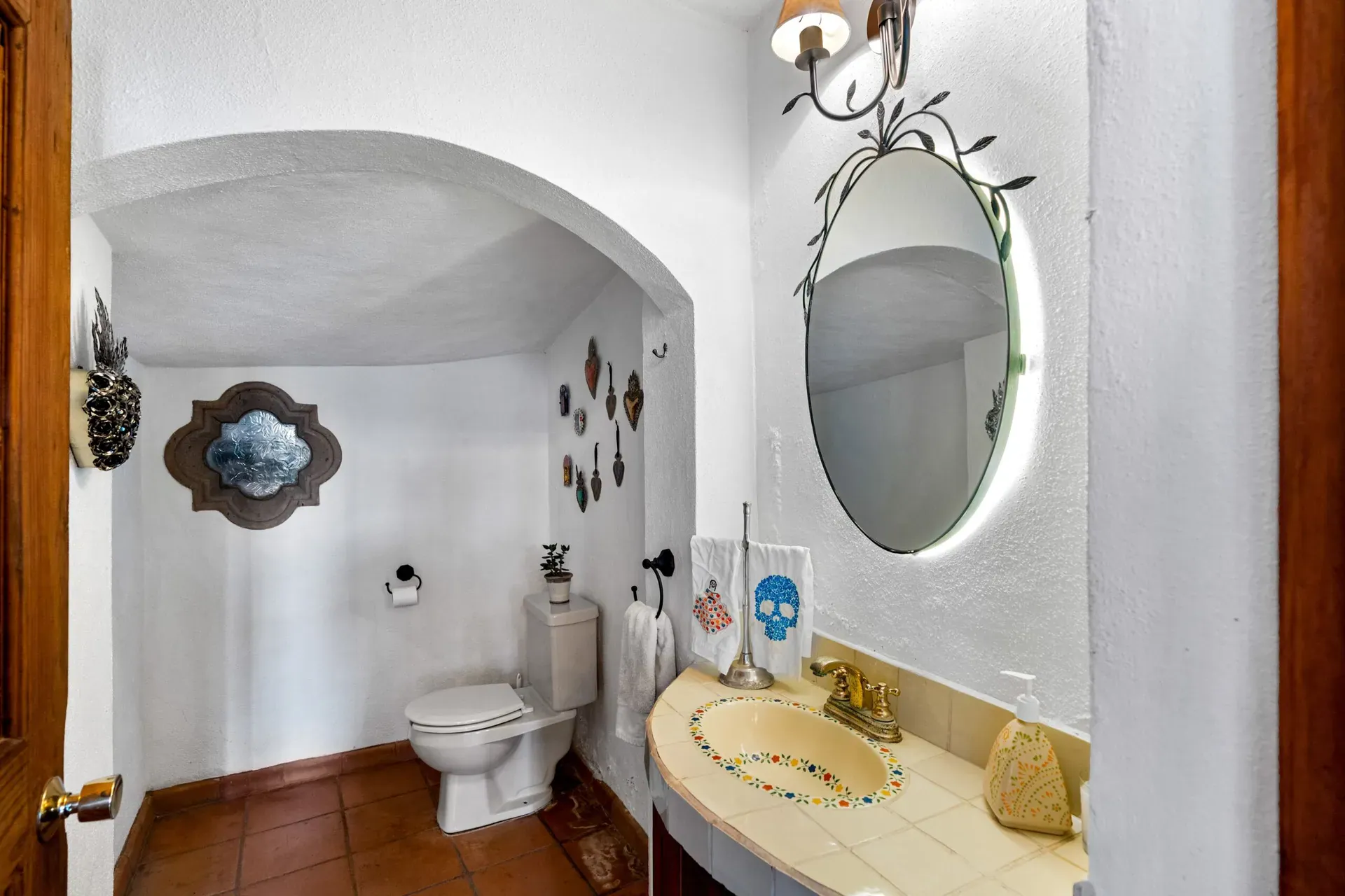 Casa Roka, powder room with an arched niche, a painted tile sink, a round lit mirror and a skull towel, San Miguel de Allende