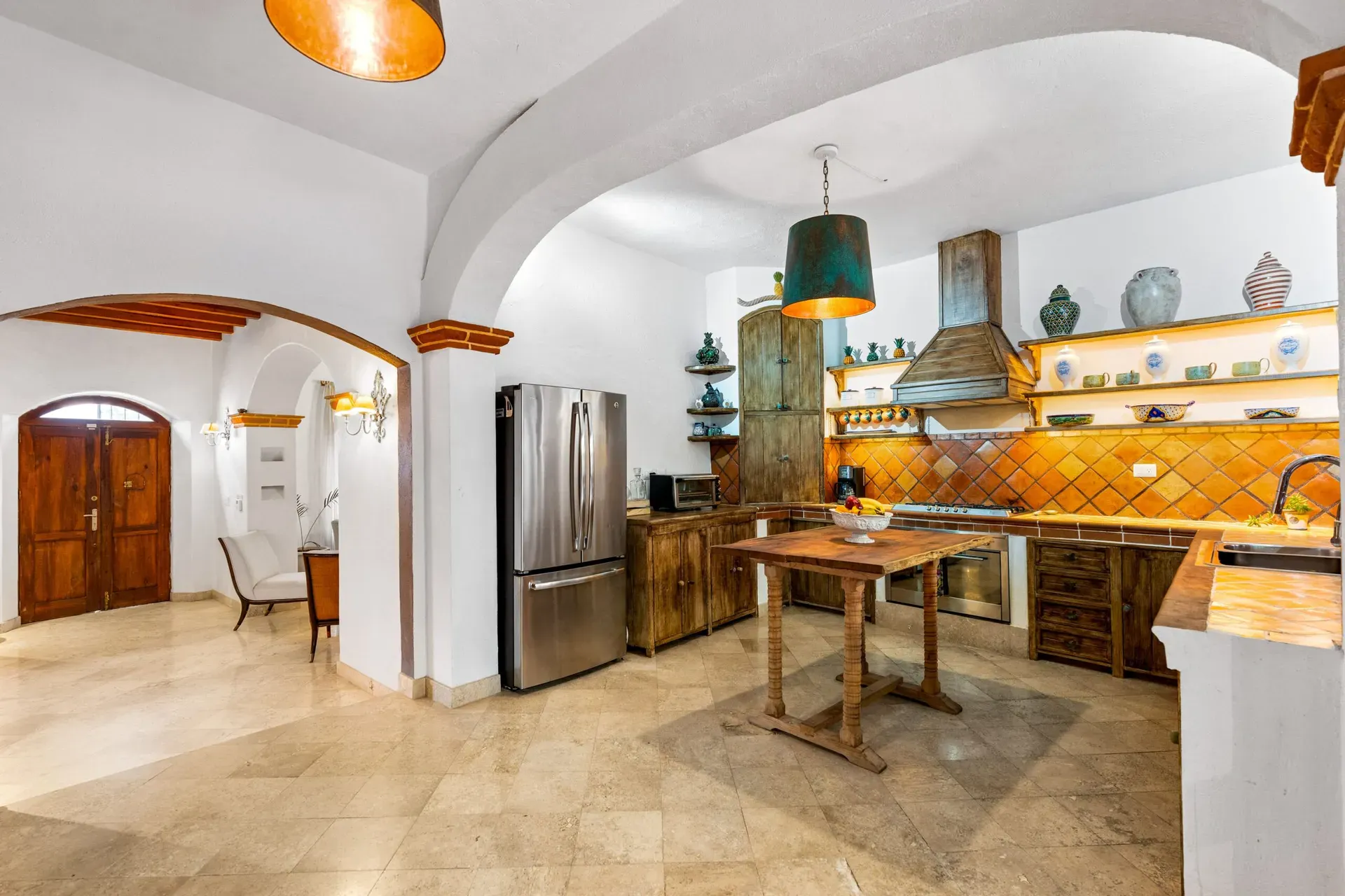 Casa Roka, kitchen with a stainless refrigerator, a wood island, a rustic hood and an arched passage to the entry, San Miguel de Allende