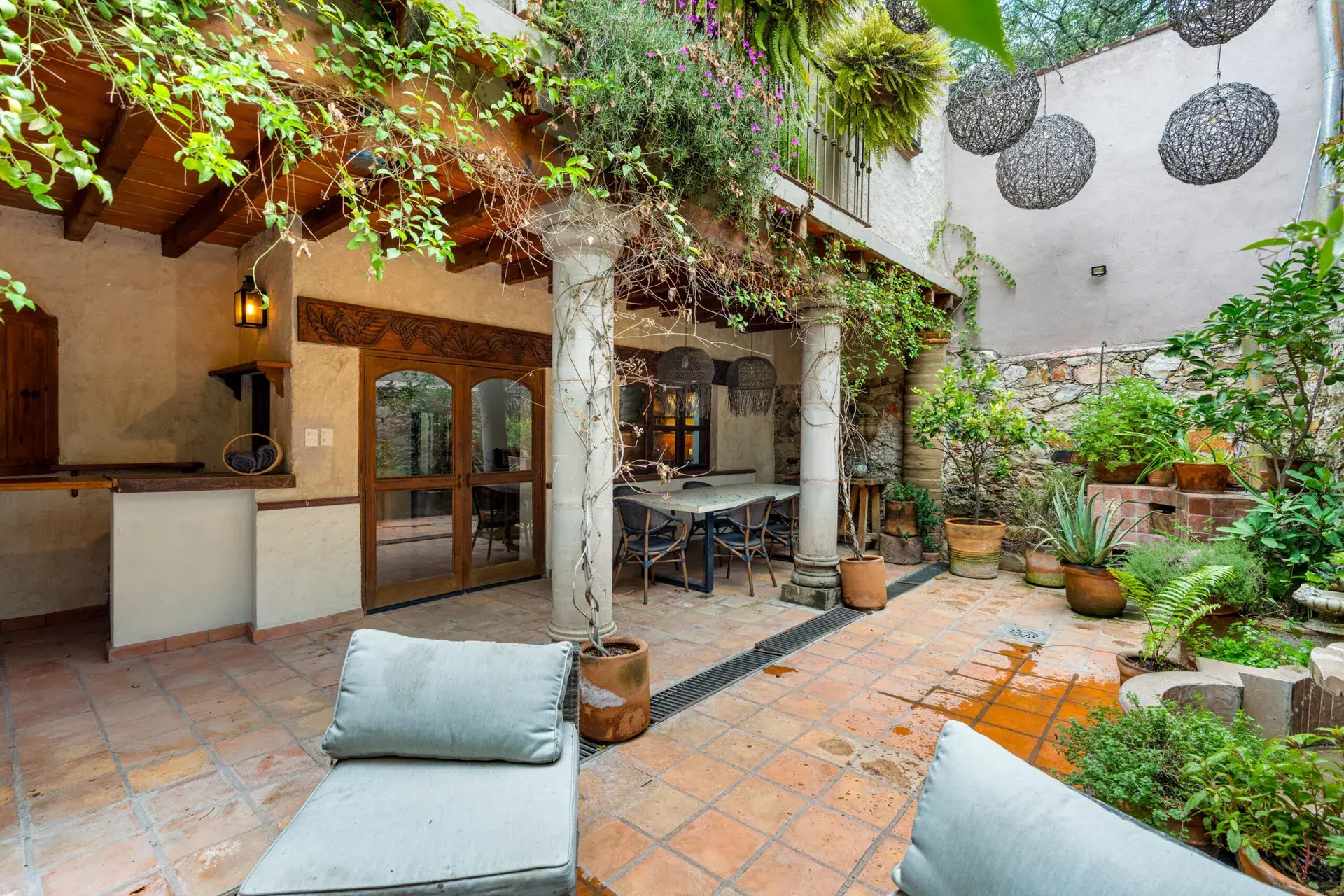 Casa Roka, courtyard with ivy, a stone fountain, hanging woven lamps, a lounge chair and an outdoor kitchen, San Miguel de Allende