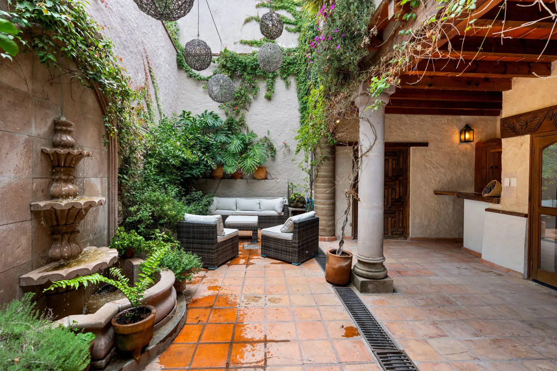 Casa Roka, courtyard garden with a tiered stone wall fountain, wicker armchairs, stone columns and tile floors, San Miguel de Allende