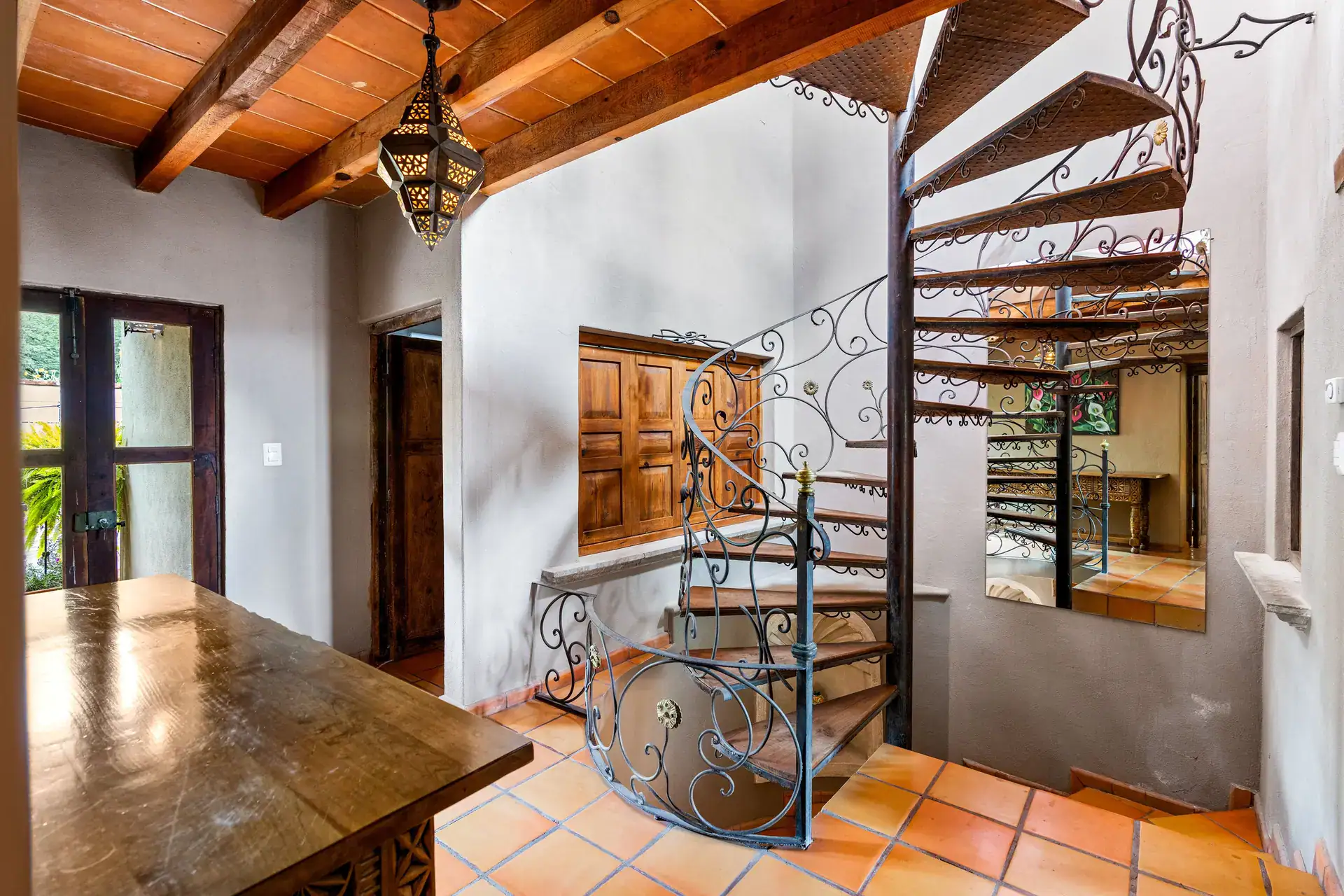 Casa Roka, spiral wrought-iron staircase with a wood-framed window and a carved wood table, San Miguel de Allende
