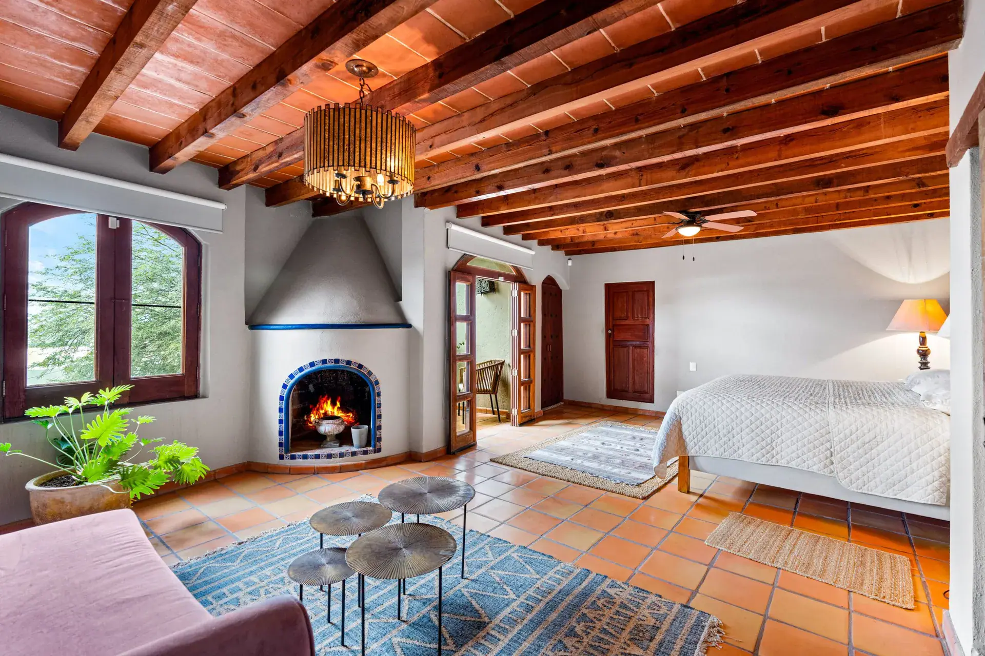 Casa Roka, suite with a corner fireplace, a bed, a purple sofa and a wood beam ceiling with a bamboo chandelier, San Miguel de Allende