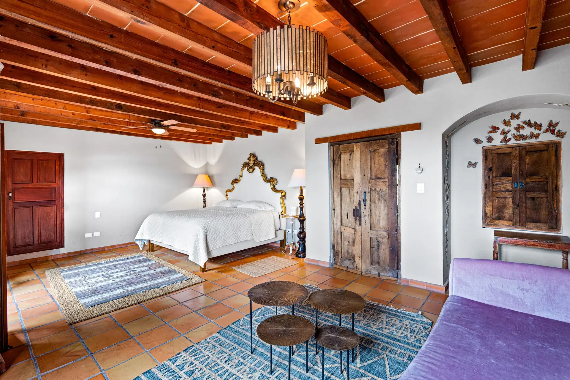 Casa Roka, bedroom with a gold ornate headboard, a purple chaise, carved wood doors and a beamed ceiling, San Miguel de Allende