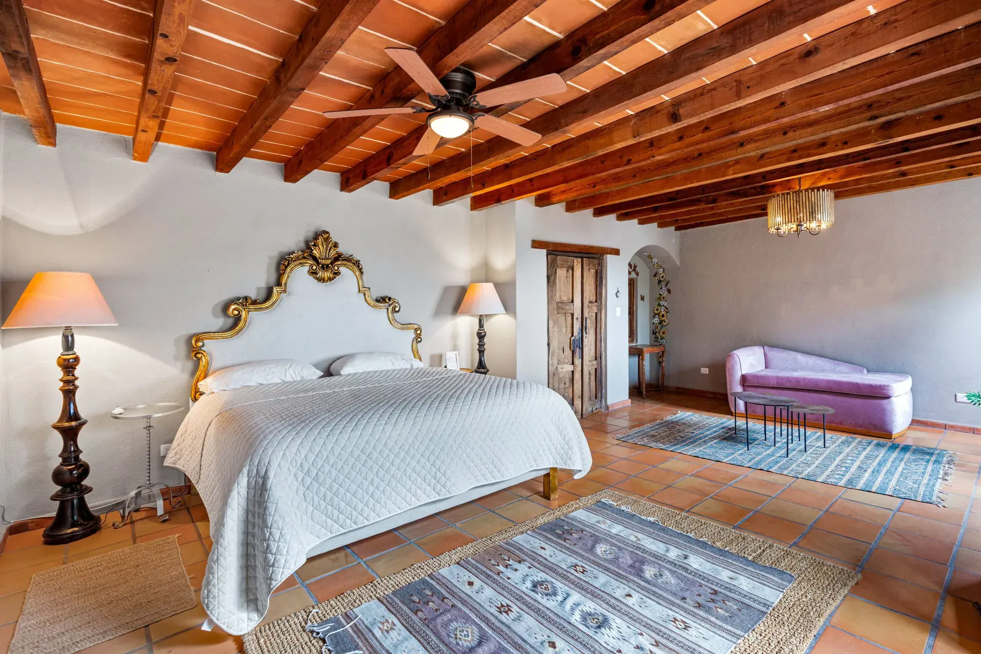 Casa Roka, bedroom with a gold ornate headboard, a pale purple chaise and a wood beam ceiling, San Miguel de Allende