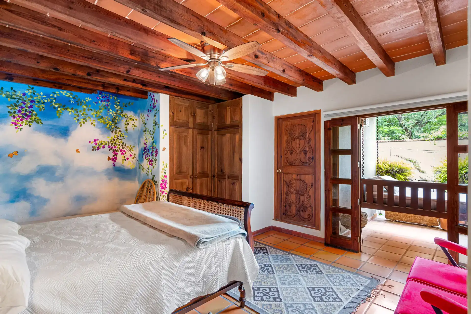 Casa Roka, bedroom with a painted blue sky mural, a cane-back bed and a balcony door, San Miguel de Allende
