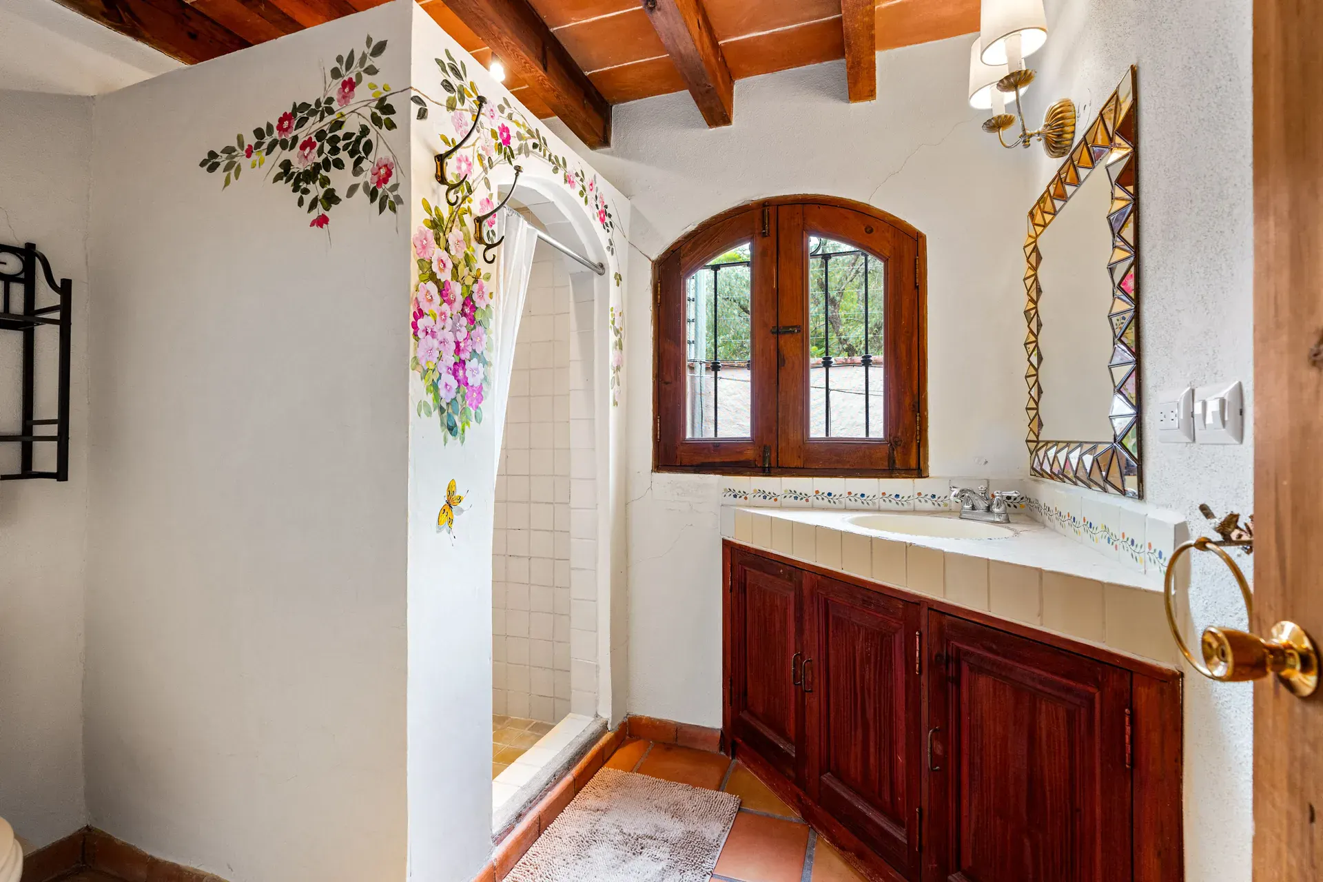 Casa Roka, bathroom with a hand-painted flower mural, an arched window, a tiled vanity and a shower, San Miguel de Allende