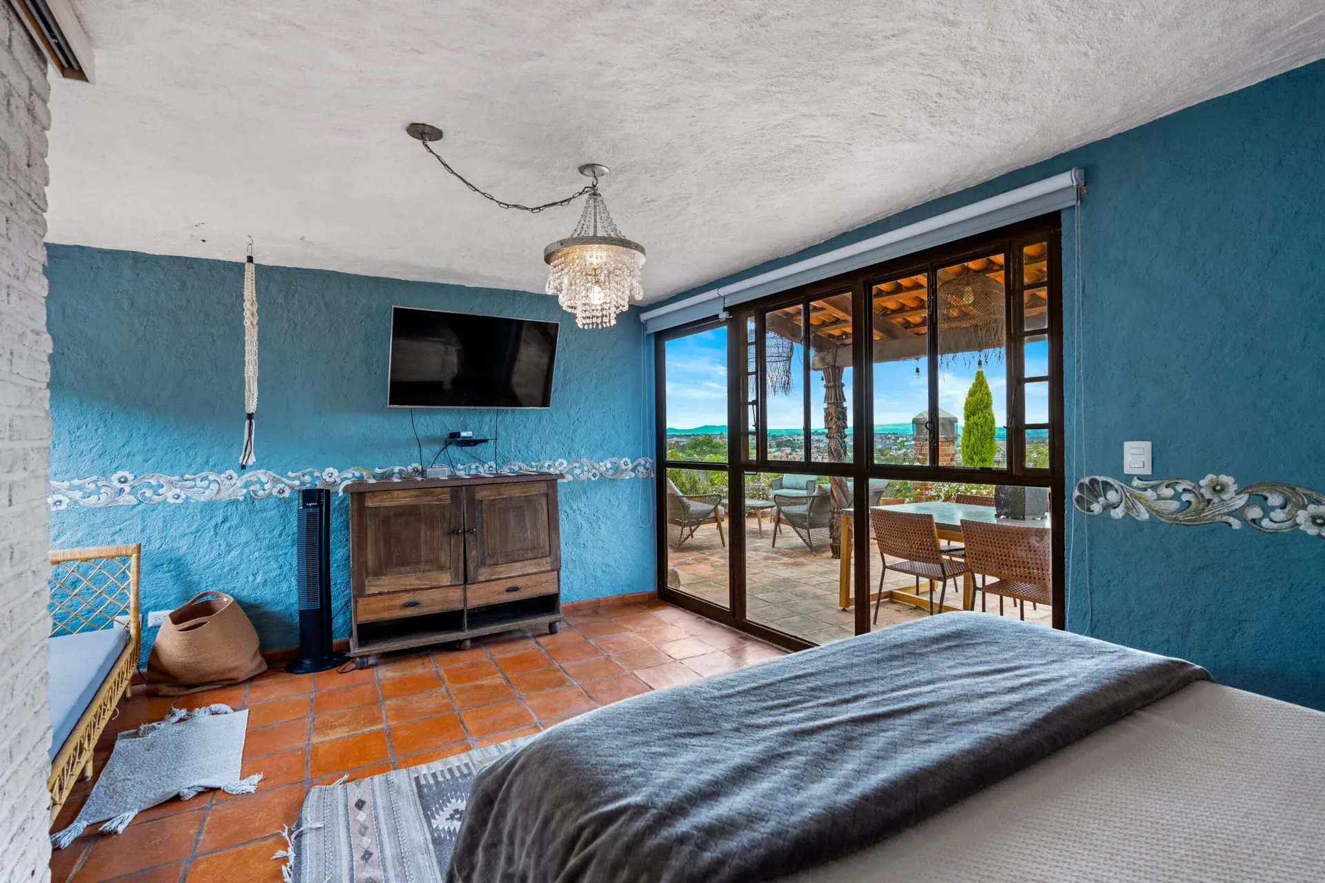 Casa Roka, bedroom with blue walls, a wall-mounted television and glass doors to a terrace overlooking the hills, San Miguel de Allende