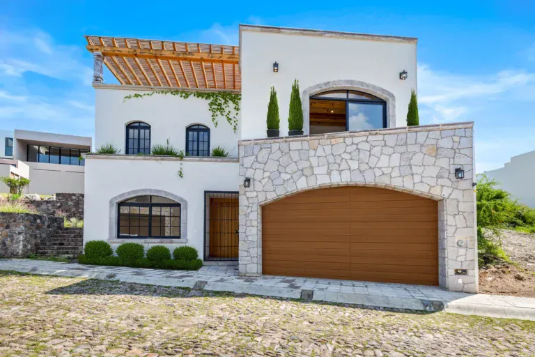 Casa Ronda, white two-story house with a stone-clad garage, an arched balcony window, a rooftop pergola and a wood garage door, San Miguel de Allende