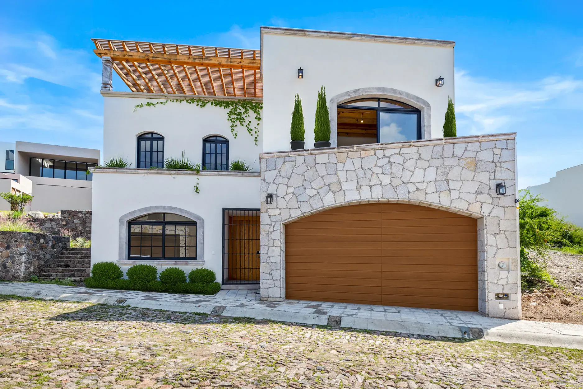 Casa Ronda, white two-story house with a stone-clad garage, an arched balcony window, a rooftop pergola and a wood garage door, San Miguel de Allende