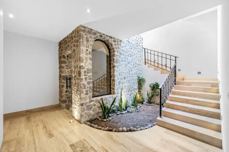 Casa Ronda, stone-walled stair core with an arched window, a gravel planter, a wood stair with an iron railing and a pale wood floor, San Miguel de Allende
