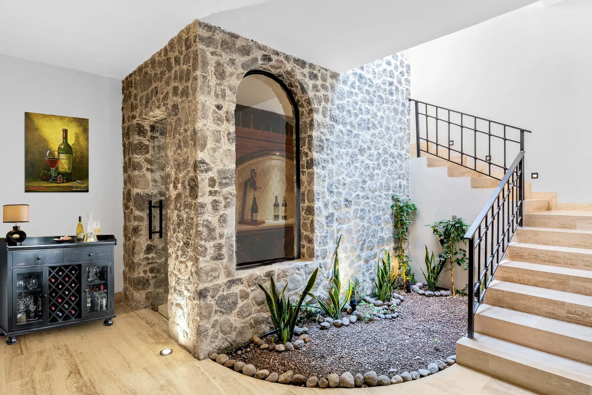 Casa Ronda, stair hall with a stone arched window, a gravel planter and a wine bar cabinet with a painting of wine bottles, San Miguel de Allende
