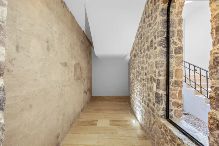 Casa Ronda, narrow passage beside a stone wall with a large black-framed window onto the staircase, San Miguel de Allende
