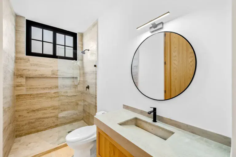 Casa Ronda, bathroom with a travertine shower, a round black mirror, a stone sink and a wood vanity, San Miguel de Allende