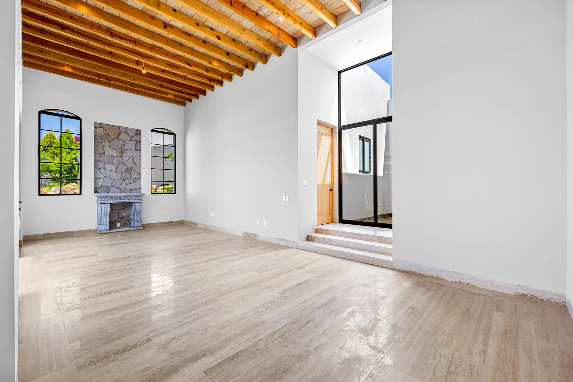 Casa Ronda, empty living area with a stone fireplace, arched windows, a wood beam ceiling and steps to a landing, San Miguel de Allende