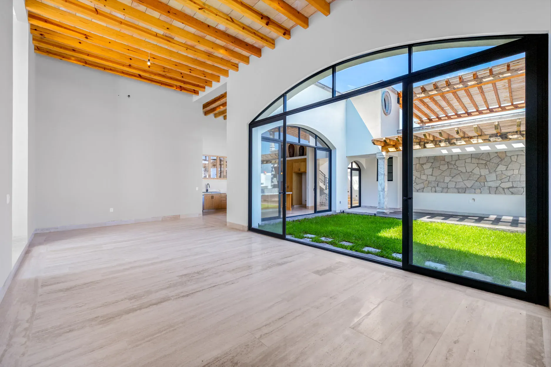 Casa Ronda, empty living room with a wood beam ceiling and a large arched glass wall to the courtyard lawn, San Miguel de Allende