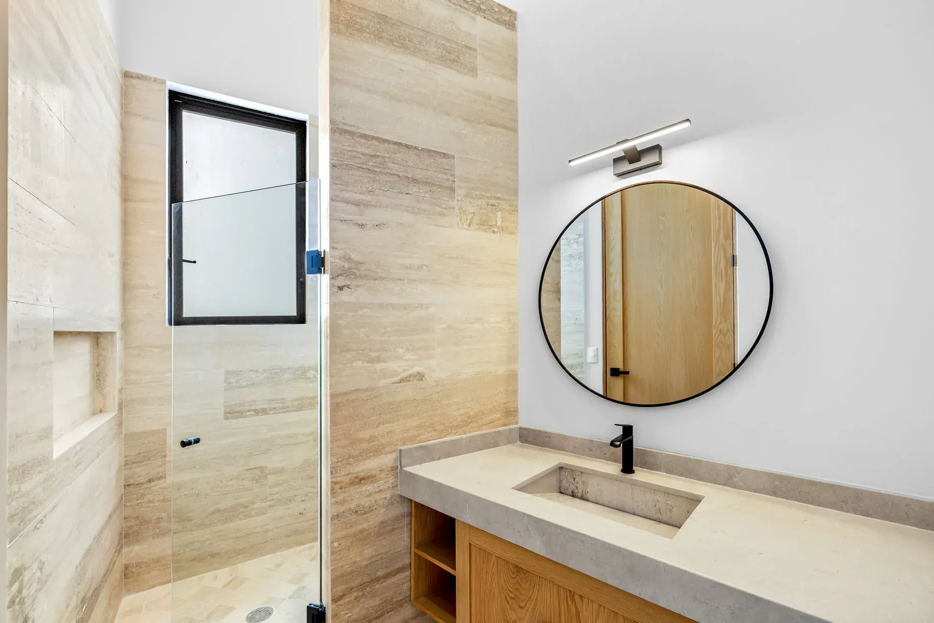 Casa Ronda, bathroom with a travertine shower, a round black mirror and a wood vanity with a stone top, San Miguel de Allende